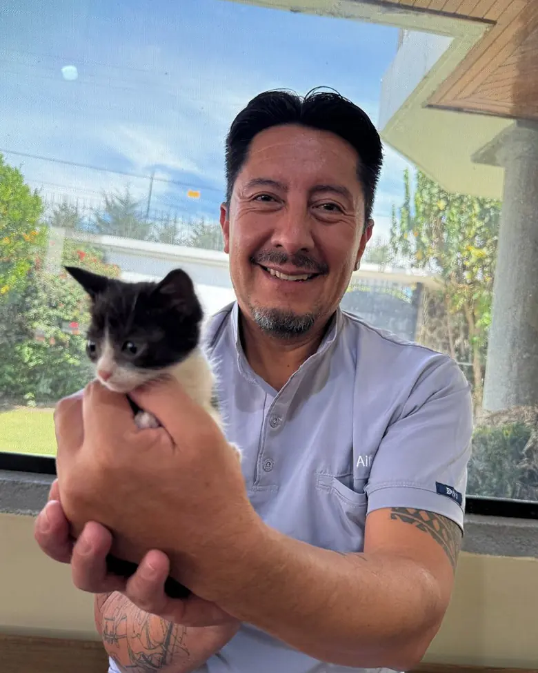 Alfredo Salgado sonríe con un gatito blanco y negro en las manos.